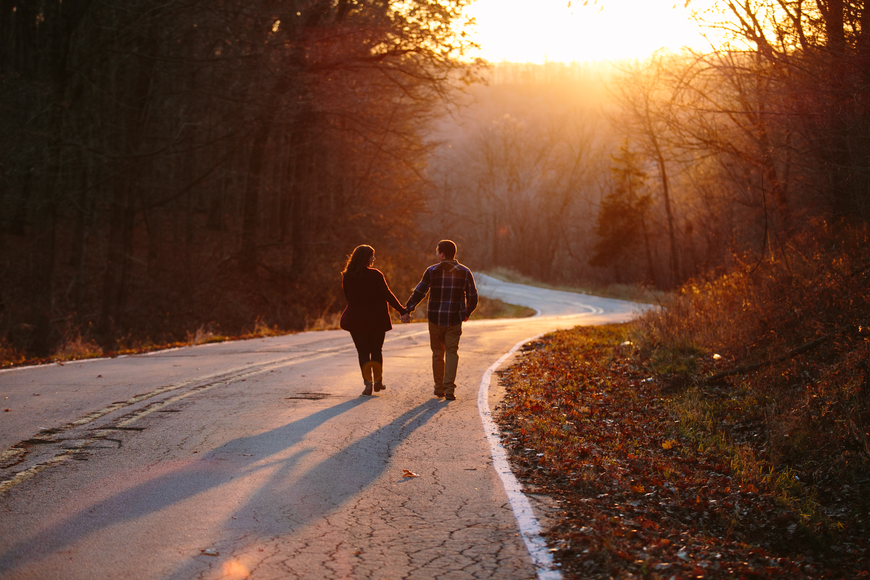 couple walking down a road at sunset, iowa farm engagement session by catherine furlin photography