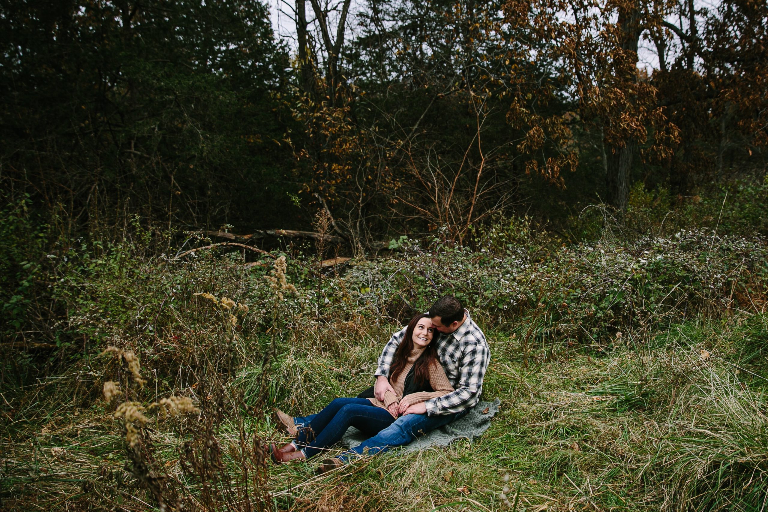 iowa couple cuddles together sitting in long grass during engagement session