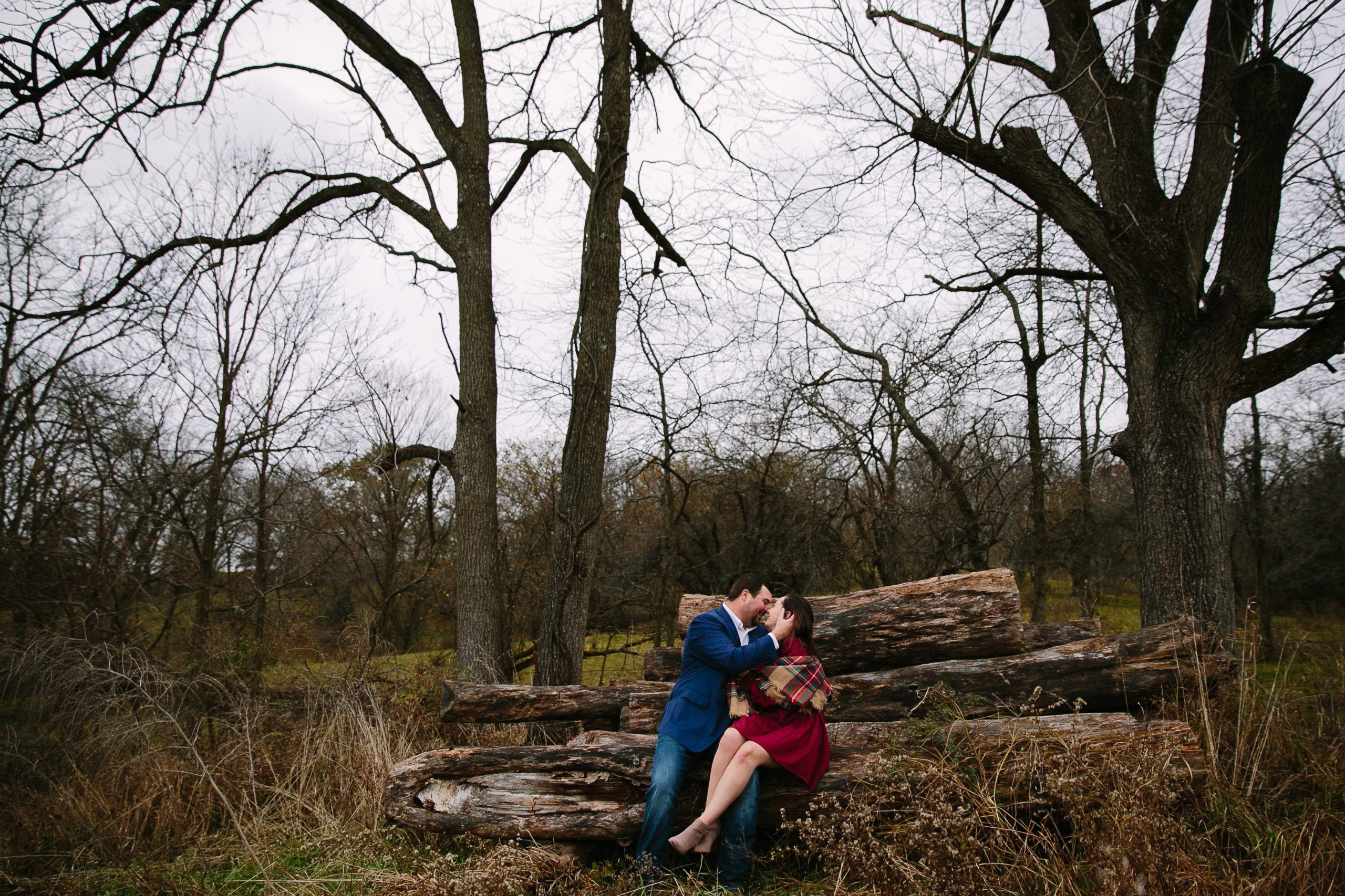 couple sitting on a pile of timber during iowa engagement session