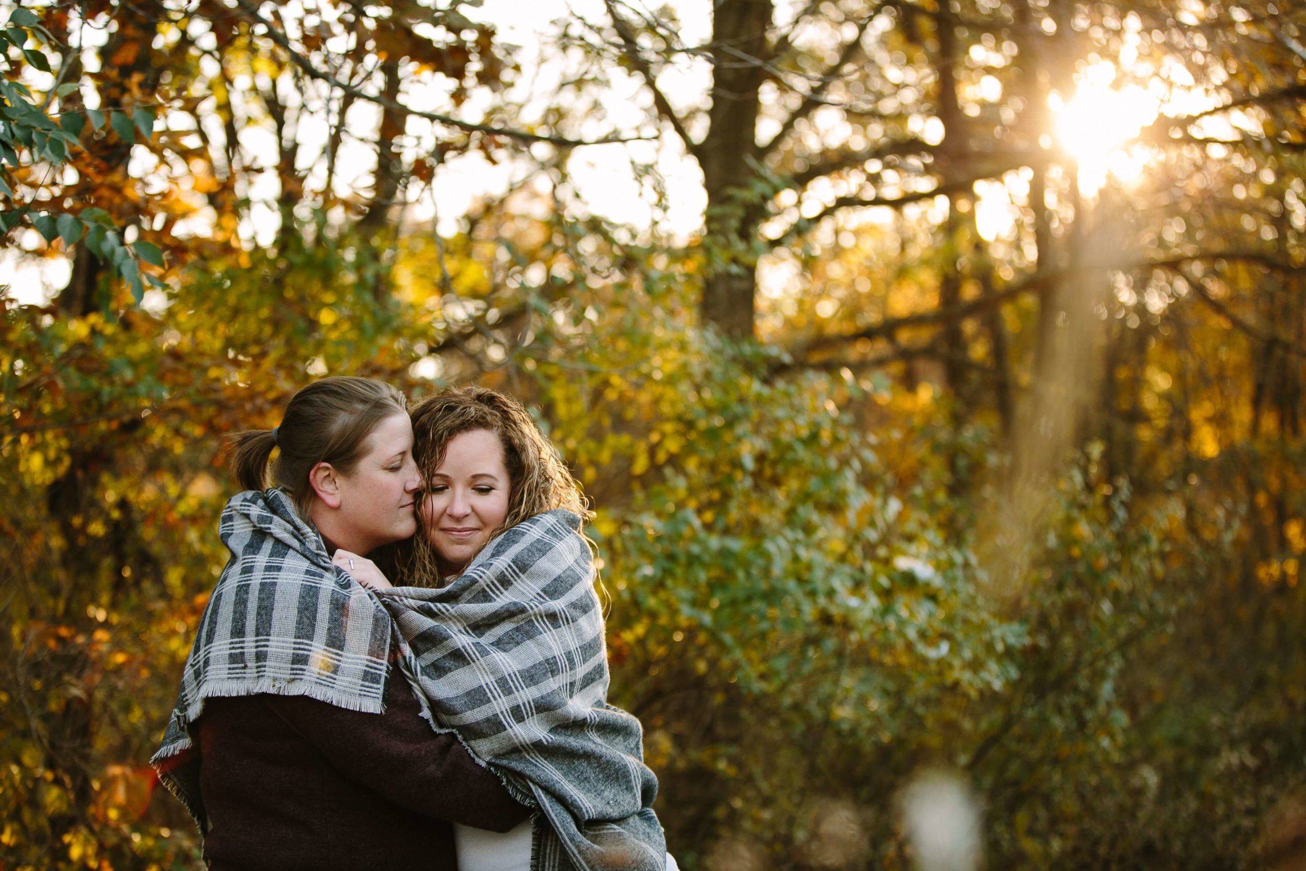 couple cuddling in a blanket during their fall engagement session in iowa