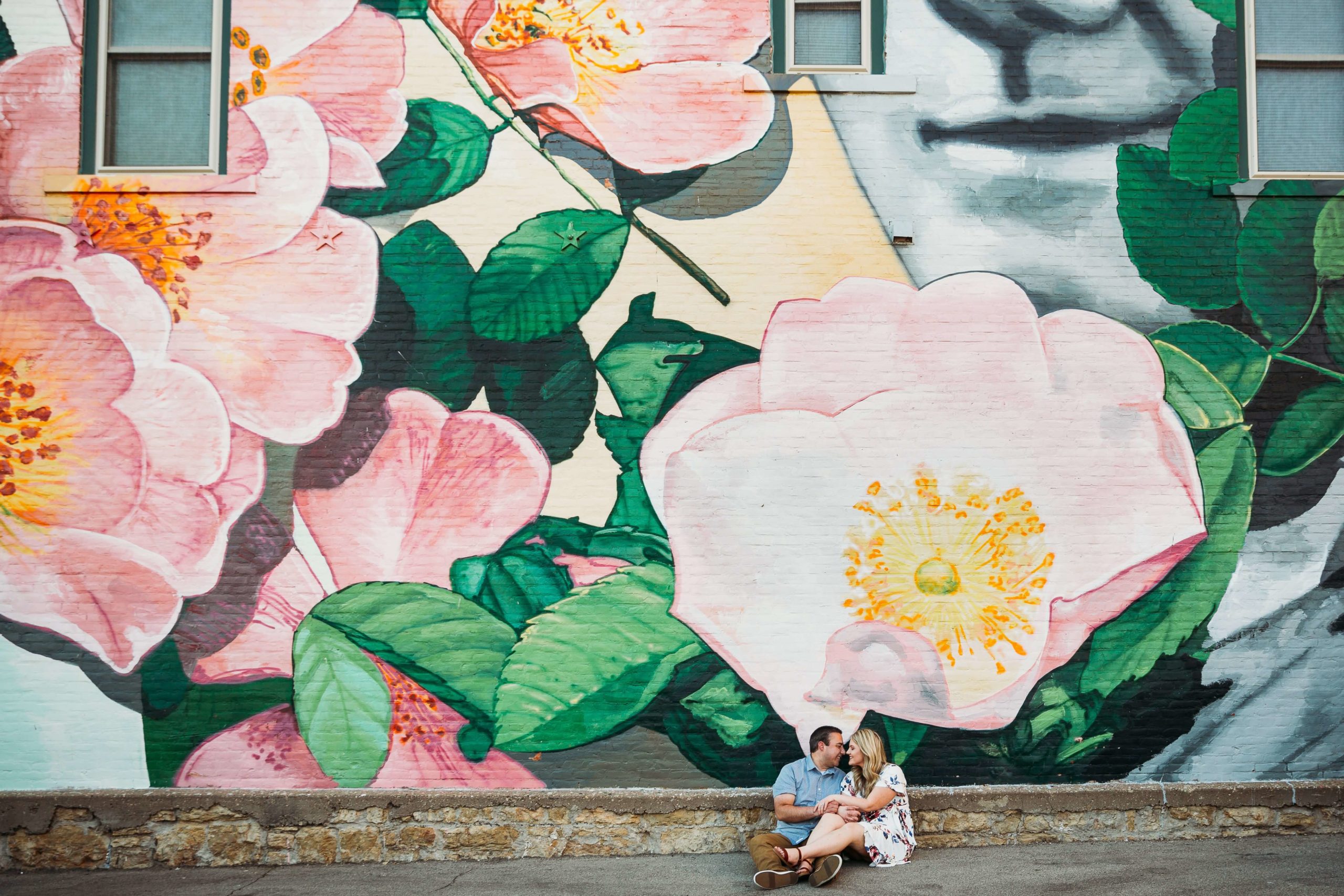 engaged couple sitting in front of a mural in downtown dubuque