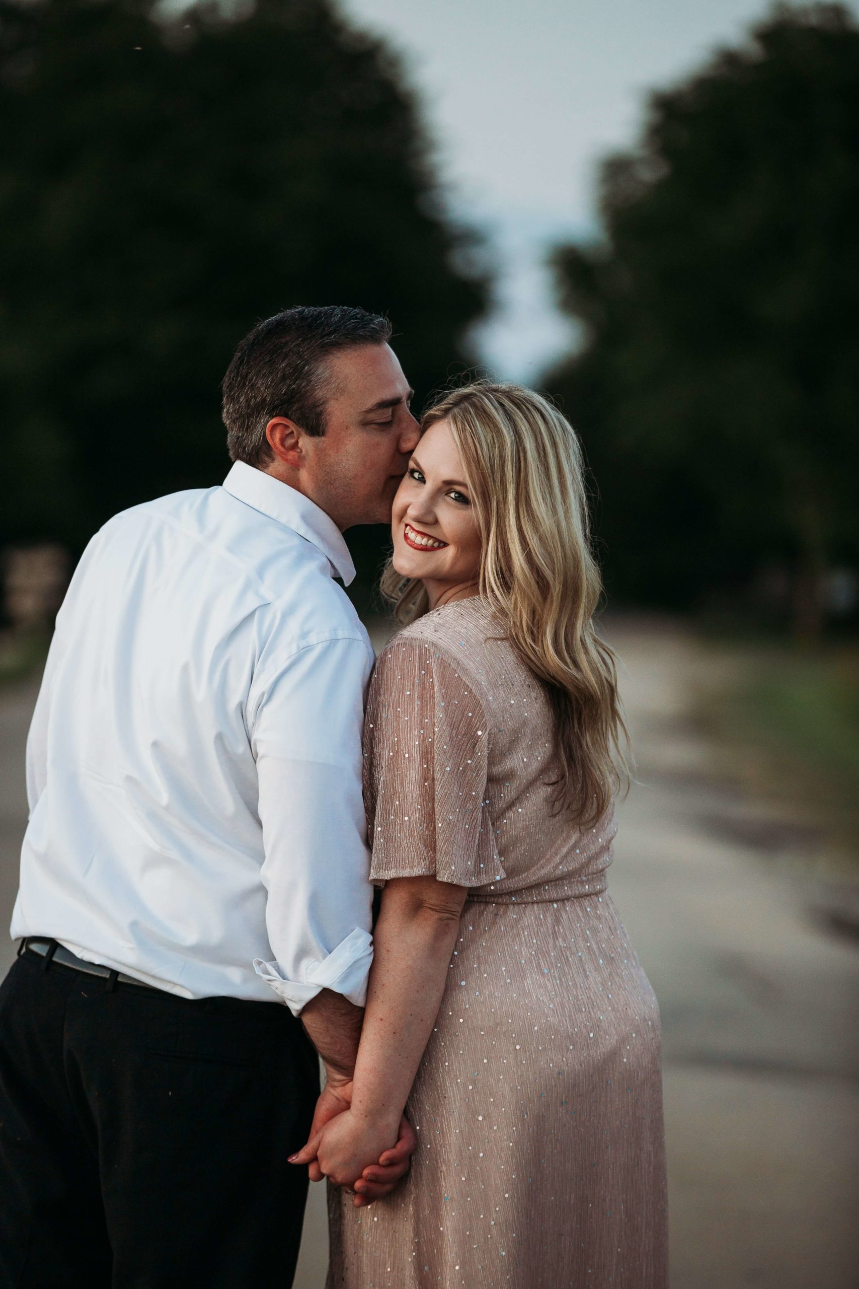 woman looking over her shoulder while her fiance kissing her head during their engagement photos